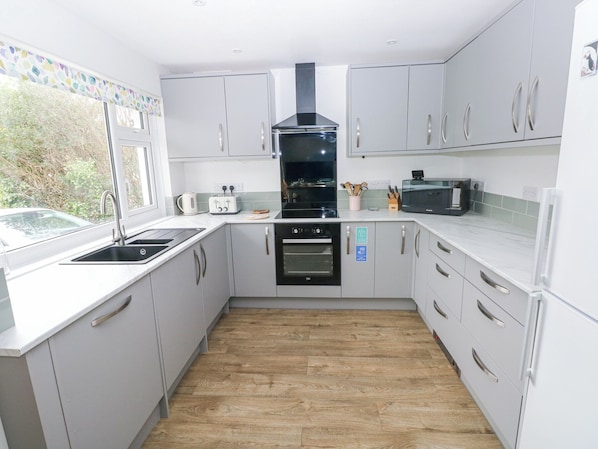A modern kitchen with white cabinets, a black stove, and a window overlooking greenery.