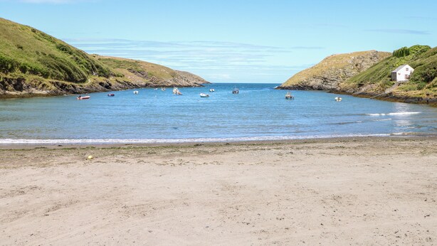 A coastal beach with boats, a white building, and grassy hills. - Chalfonts Cottage (Haverfordwest)