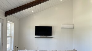 A modern living room with a large gray sectional sofa, a mounted flat-screen TV, and a wooden ceiling beam.