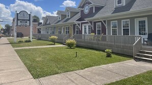 A row of single-story houses with a clock on the front of the central house, a wooden fence, and a sign indicating a vacancy for a suite apartment.