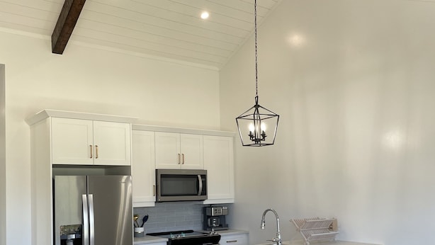 A modern kitchen with white cabinetry, stainless steel appliances, a central island with bar stools, and a hanging light fixture.