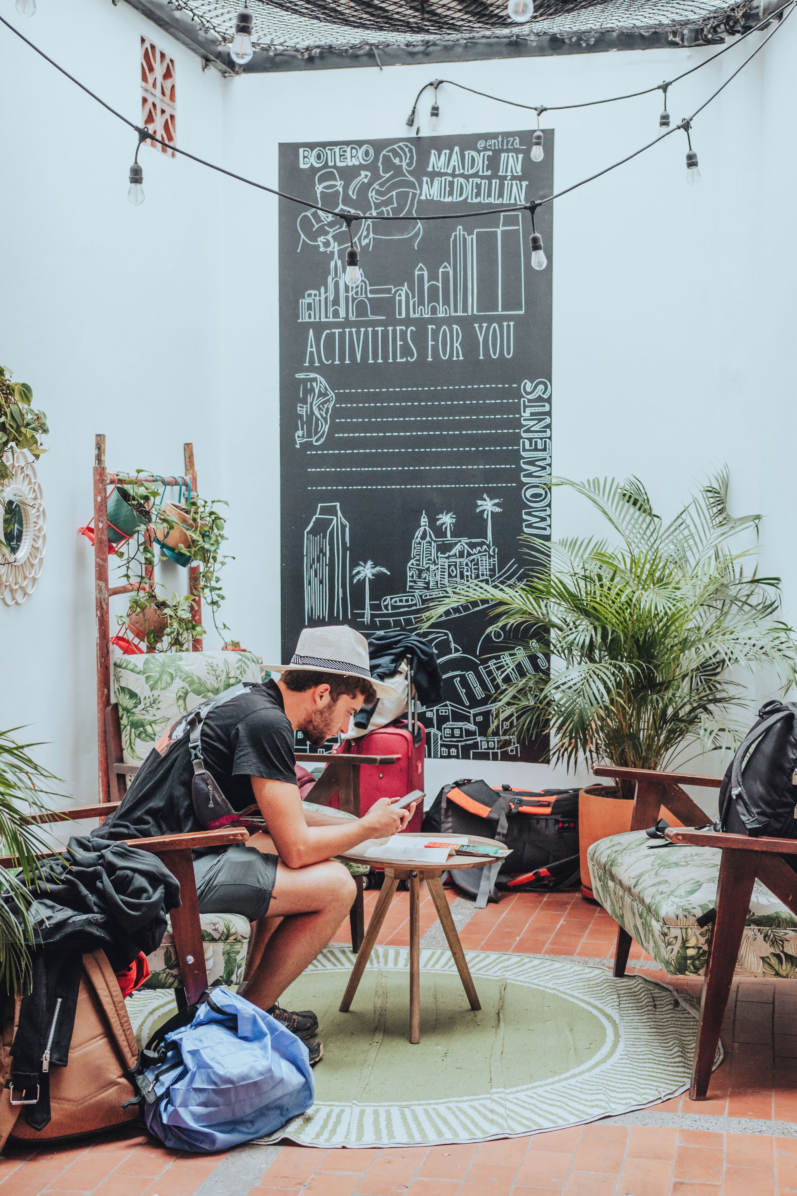 Una persona sentada en una mesa con una computadora portátil, rodeada de plantas y un cartel en la pared.