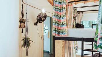 Dormitorio con literas, ventilador, cortinas y plantas colgantes.