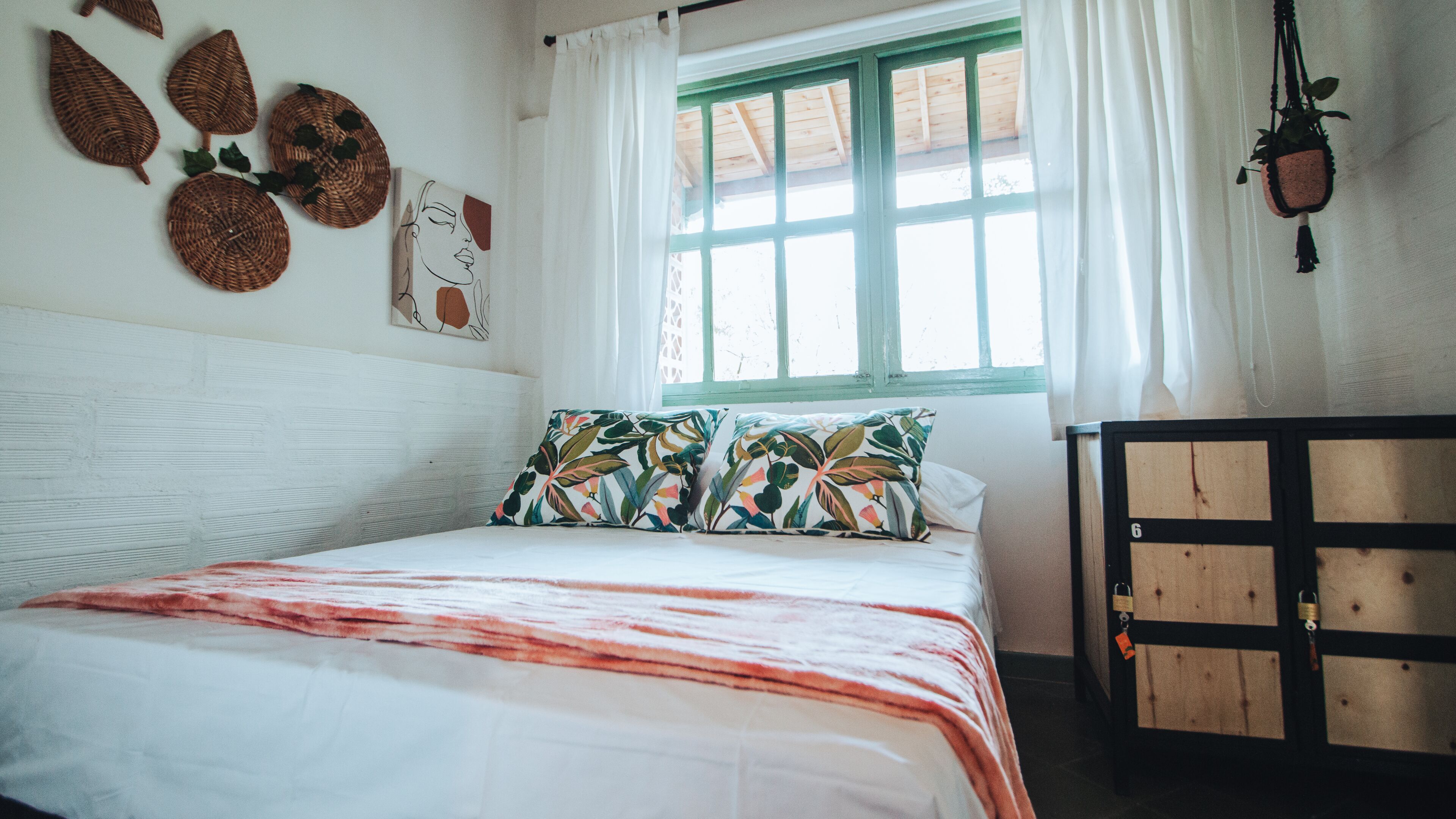 Ein Schlafzimmer mit Bett, einem fenster mit Vorhängen, einer Wand mit Dekoration und einem Holzschrank.