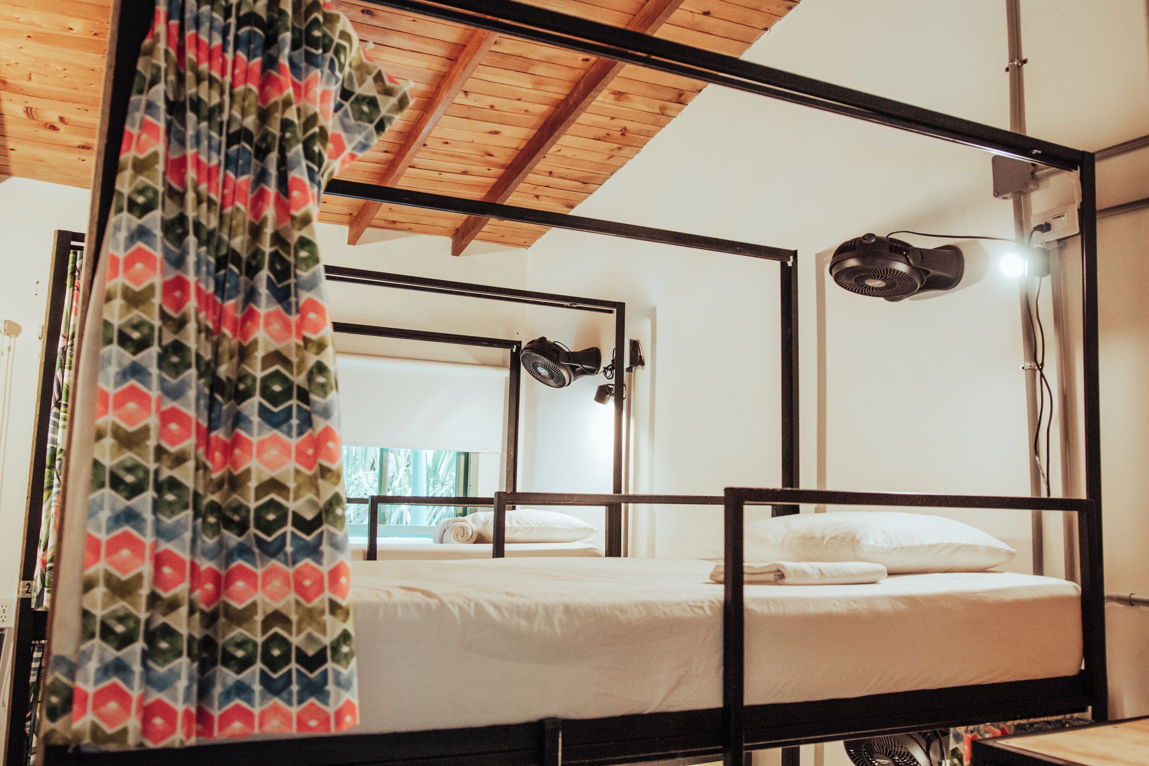 Une chambre avec un lit superposé, un plafond en bois, un ventilateur de plafond et une fenêtre avec des rideaux.