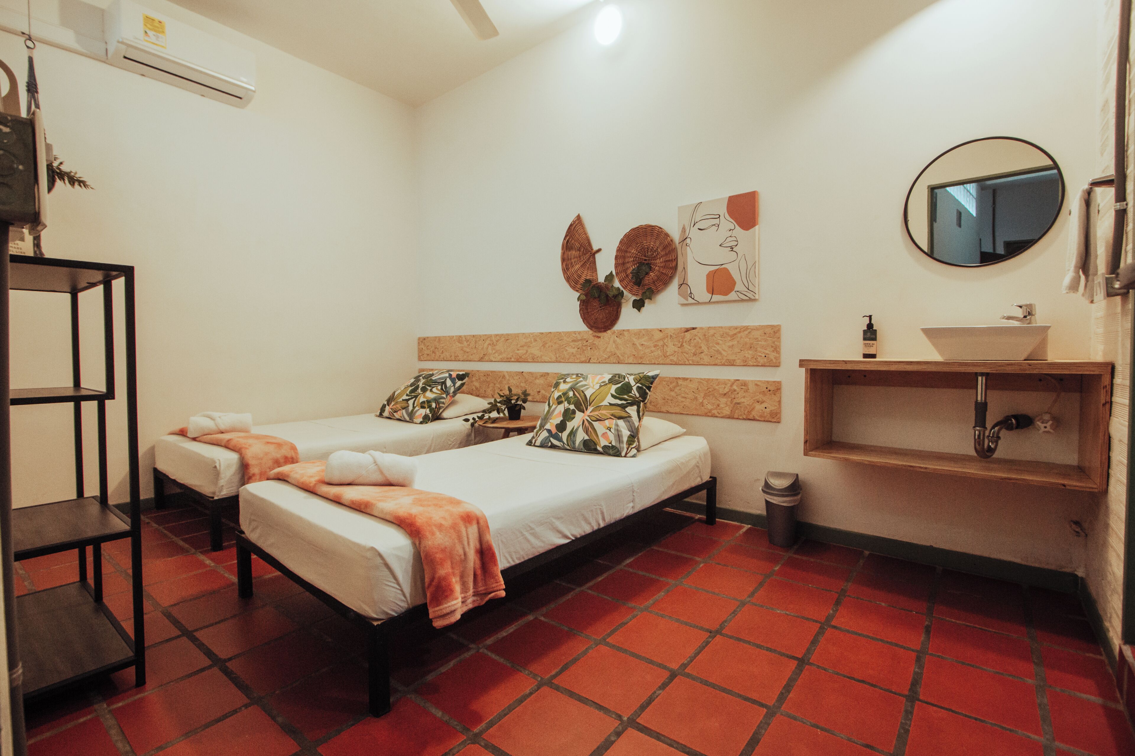 Habitación de hotel con dos camas, un lavamanos, un espejo y un cesto de basura.