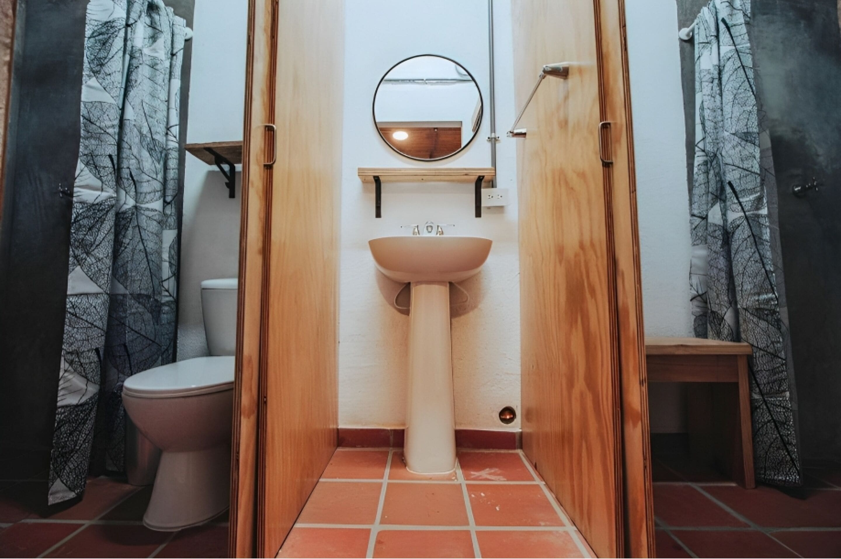 Ein Badezimmer mit Holztür, Toilette, Standwaschbecken und einem Spiegel darüber.