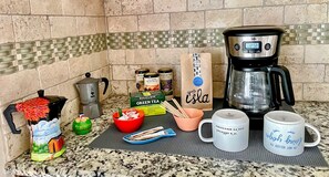 A kitchen counter with a coffee maker, tea bags, a mug, and a coffee grinder. - Comfy & spacious home (Austin)