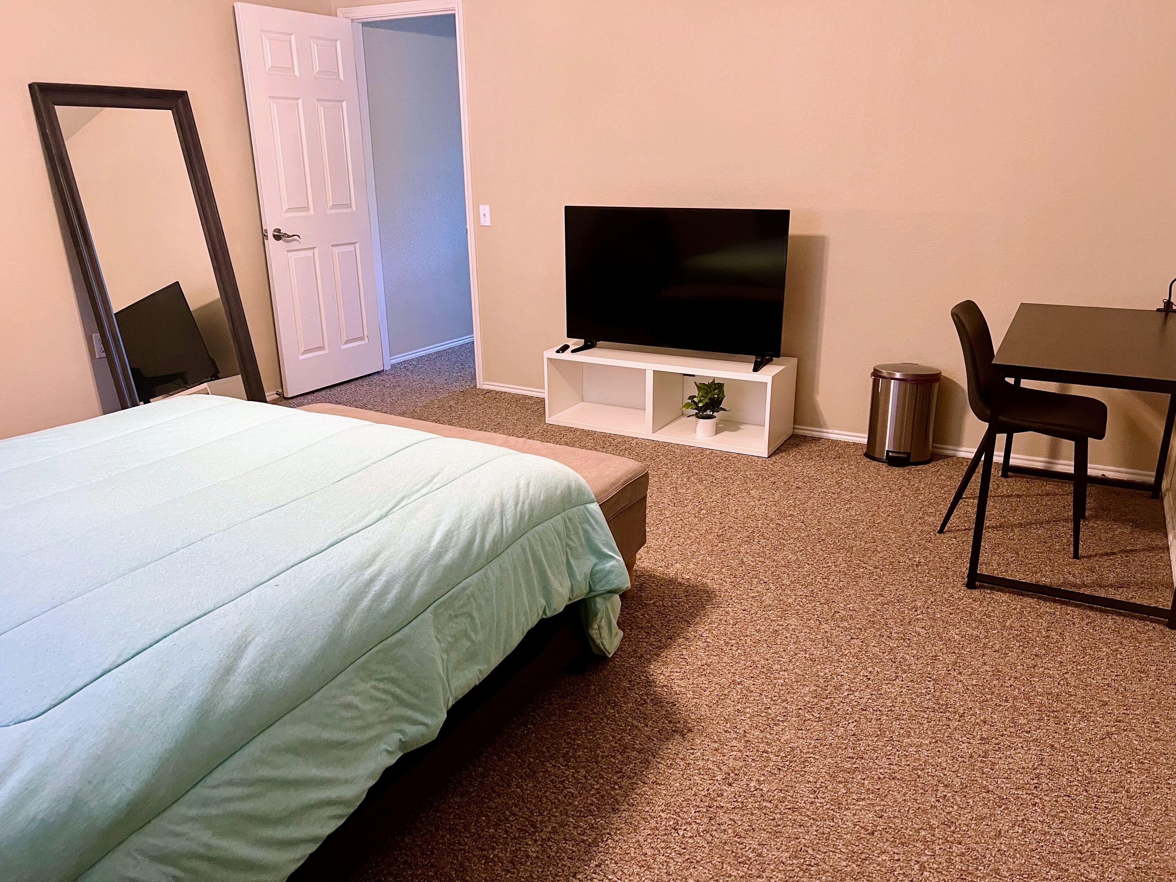 Een hotelkamer met een bed, een televisie op een standaard, een bureau met een stoel en een prullenbak.