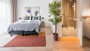 A modern bedroom with a bed, bedside tables, a potted plant, and a shower area. - Limehome Frankfurt Gutleutstraãÿe (Frankfurt)