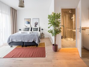 A modern bedroom with a bed, bedside tables, a potted plant, and a shower area. - Limehome Frankfurt Gutleutstraãÿe (Frankfurt)