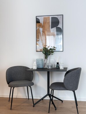 A modern room with a dark wooden floor, two grey upholstered chairs, a black metal table, and a framed abstract painting. - Limehome Frankfurt Gutleutstraãÿe (Frankfurt)