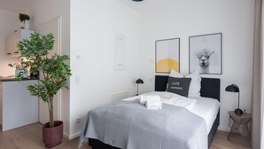 A modern hotel room with a bed, bedside tables, a potted plant, and artwork on the walls.