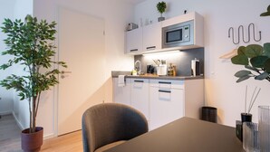 A modern kitchen with white cabinets, a microwave, and a sink. There is a dining table with chairs, a potted plant, and a vase with reeds.