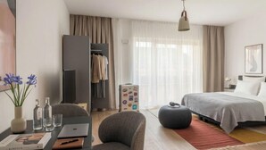 A modern hotel room with a bed, a desk with a laptop, a chair, a wardrobe, and a suitcase. - Limehome Frankfurt Gutleutstraãÿe (Frankfurt)