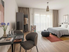 A modern hotel room with a bed, a desk with a laptop, a chair, a wardrobe, and a suitcase. - Limehome Frankfurt Gutleutstraãÿe (Frankfurt)