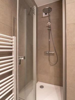 A glass-enclosed shower with a handheld showerhead, a wall-mounted faucet, and a white towel rack. - Limehome Frankfurt Gutleutstraãÿe (Frankfurt)