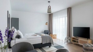 A modern hotel room with a bed, a TV, a dining area, and a window with curtains. - Limehome Frankfurt Gutleutstraãÿe (Frankfurt)