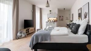 A modern bedroom with a bed, a TV, a kitchenette, and a large window. - Limehome Frankfurt Gutleutstraãÿe (Frankfurt)
