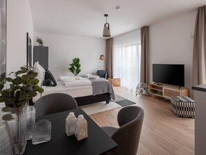 A modern hotel room with a bed, bedside table, TV, and a dining area with chairs and a table. - Limehome Frankfurt Gutleutstraãÿe (Frankfurt)