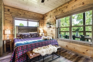 Quarto de cabana de madeira com cama, um banco, uma janela e vista para o exterior.