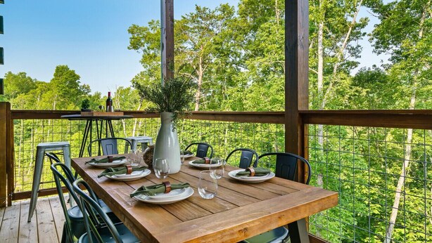 A wooden deck with a table set for dining, surrounded by chairs, and a vase with greenery. - Private Indoor Pool/Pet Stays Free/HotTub/Movie (Sevierville)