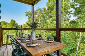 Een houten terras met een eettafel, omringd door stoelen, en een vaas met groen.