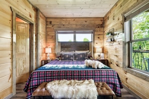 Quarto de cabana de madeira com cama, almofadas, um banco e uma janela.