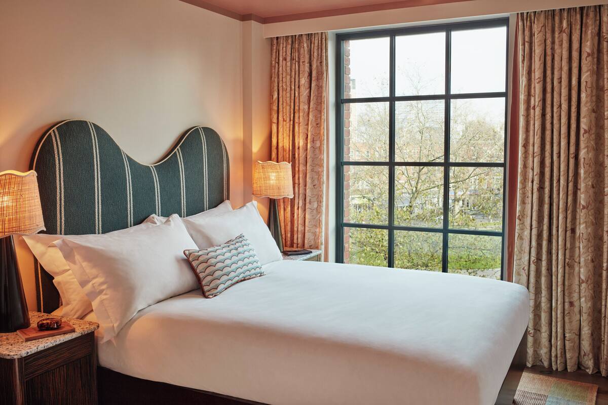 A neatly made bed with white linens and striped pillows, a headboard with vertical lines, and a nightstand with a lamp and a book.