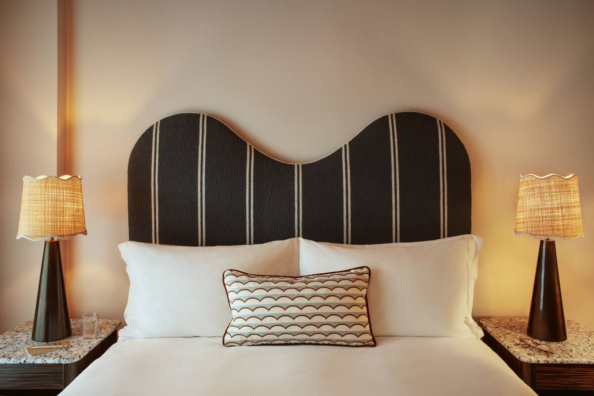 A neatly made bed with a patterned pillow, flanked by two bedside tables each with a lamp, against a wall with a striped pattern.