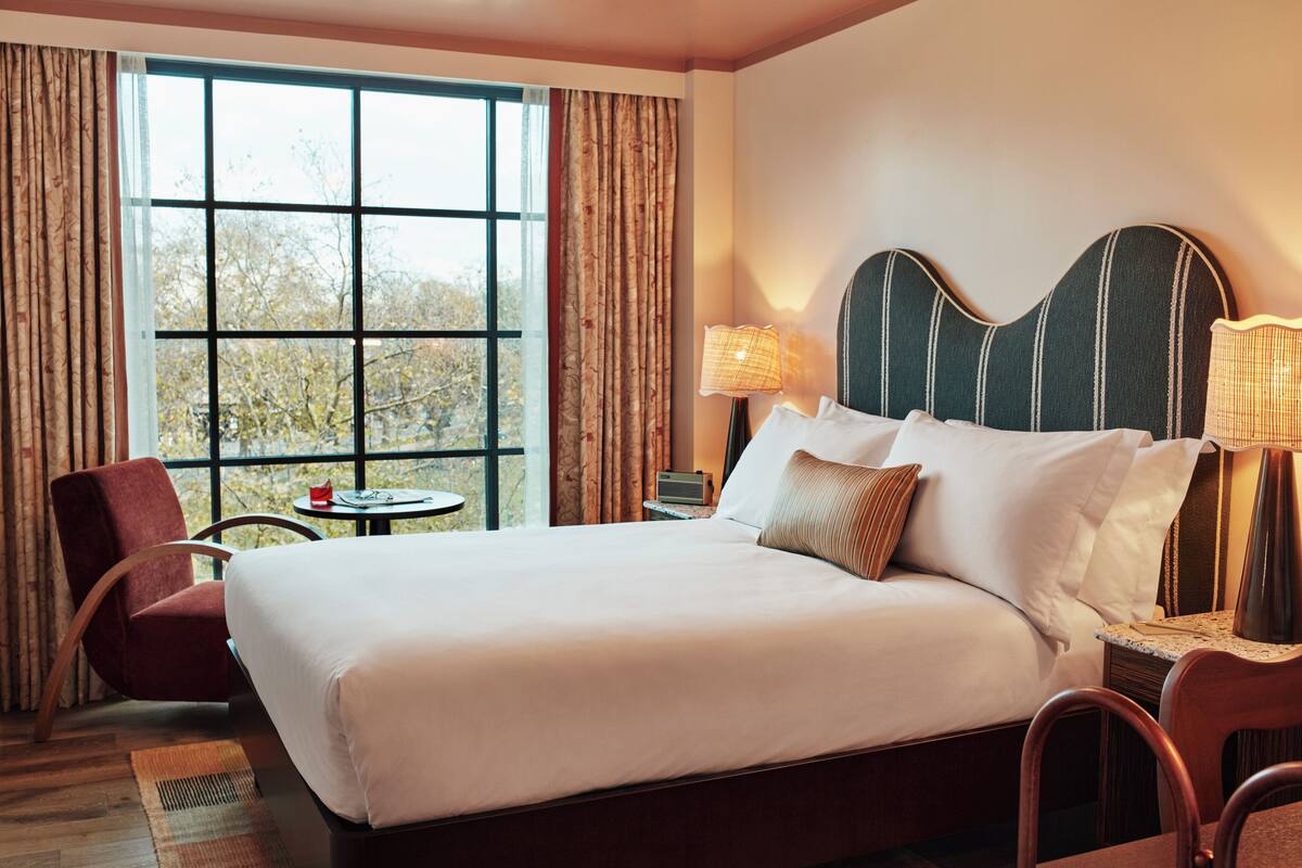 A hotel room with a large bed, a chair, a small table, and a window with curtains.