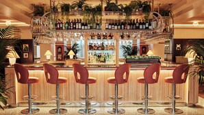 Uma área de bar com vários bancos, um suporte para vinhos e diversas garrafas.