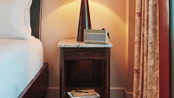 A neatly made bed with pillows, a small bedside table with a lamp, a stack of books, and a curtain.