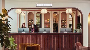 Uma mesa de recepção com computadores, uma placa com a inscrição 'CHECK IN' e um design de painel de madeira.
