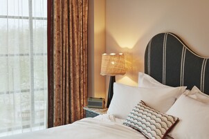 A neatly made bed with white linens and patterned pillows, a bedside lamp, and a radio on a nightstand.