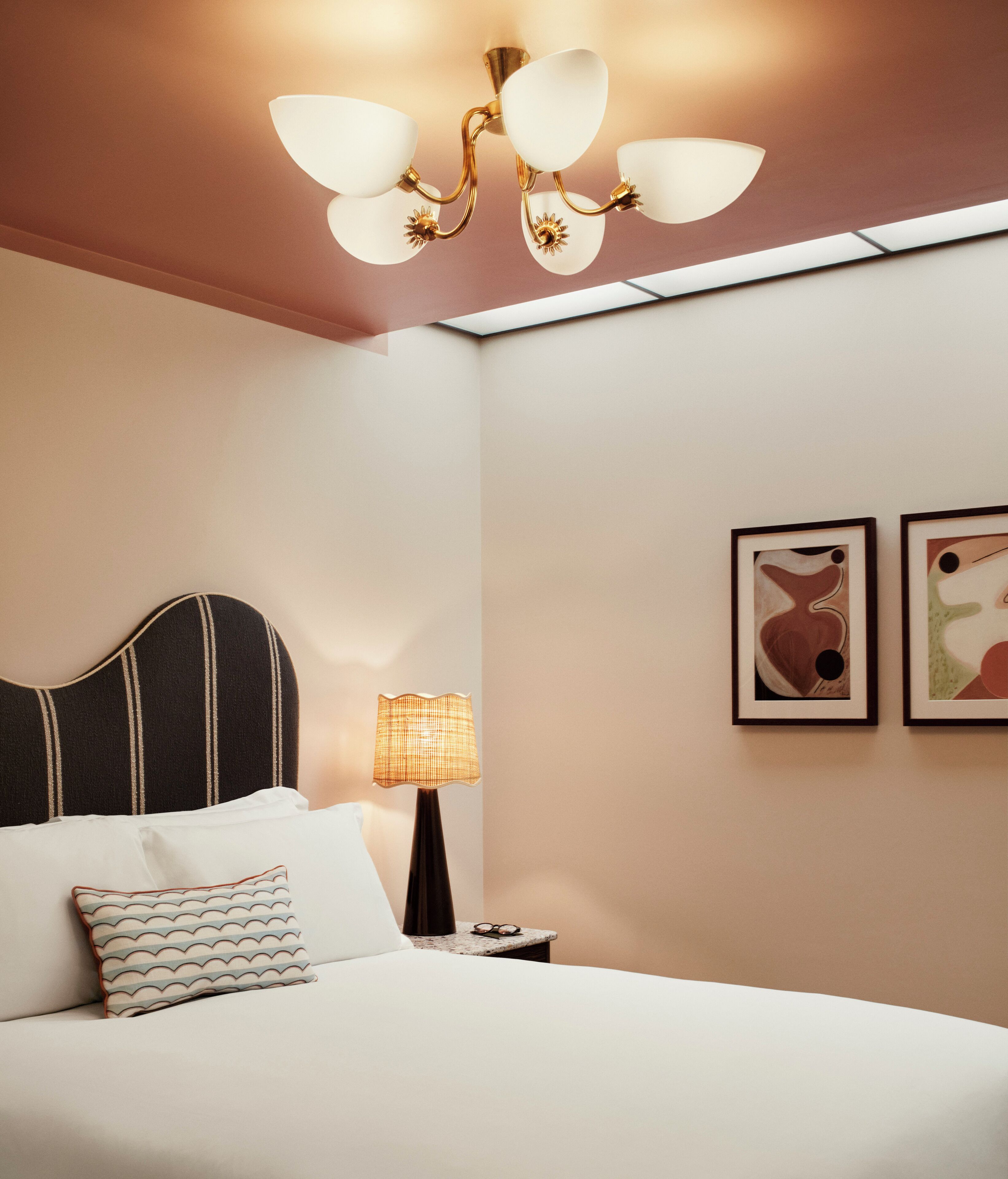 A neatly made bed with a striped headboard, a bedside lamp, and two framed abstract artworks on the wall.