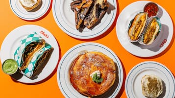 A variety of breakfast dishes on white plates with blue rims, including pancakes, French toast, and omelets, on an orange table.