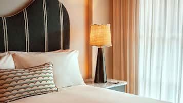 Una cama bien tendida con un cabecero a rayas, una almohada estampada y una lámpara en una mesita de noche.