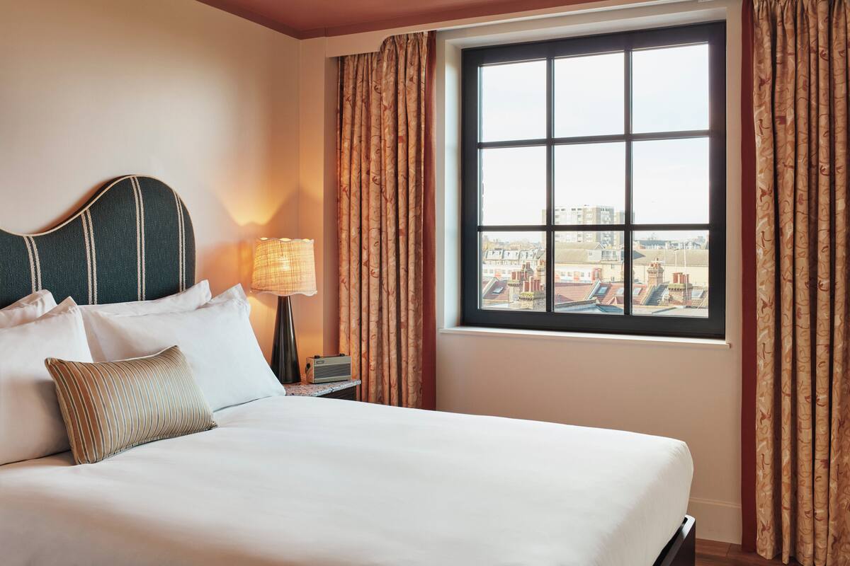 A hotel room with a large bed, a nightstand with a lamp, and a window with curtains.