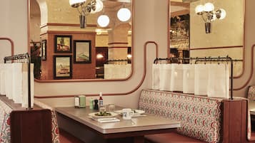 Een restaurant met een zithoek in loungeruimte, een lange tafel en een bar die in de reflectie zichtbaar is.