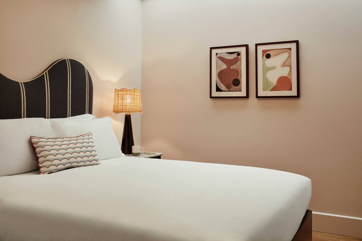 A neatly made bed with a striped pillow, a bedside lamp, and two abstract wall art pieces.