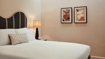Una cama bien hecha con un almohadón a rayas, una lámpara de noche y dos obras de arte abstracto en la pared.