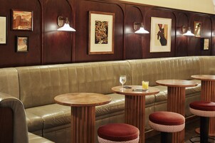 A restaurant interior with a leather booth seating, wooden tables, and red cushioned stools.