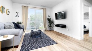 A modern living room with a grey sofa, a black coffee table, and a large window with curtains. - King Bed + Sofa I Walk DT + Front St (Traverse City)
