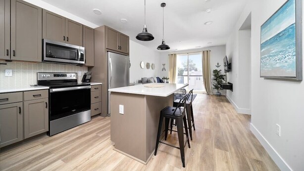 A modern kitchen with a central island, stainless steel appliances, and a dining area with bar stools. - King Bed + Sofa I Walk DT + Front St (Traverse City)