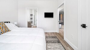Una habitación de hotel moderna con una cama grande, un televisor de pantalla plana montado en la pared y un vestidor.