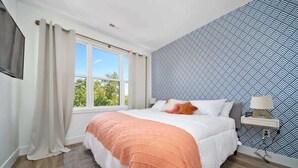 Une chambre à coucher avec un grand lit, une fenêtre avec des rideaux, un mur à motifs et une table de chevet avec une lampe.