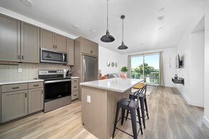A modern kitchen with stainless steel appliances, a large island, and a view of the outdoors. - Front Street Stay I King + Sofa I Walk Shops (Traverse City)