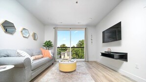 Un salon moderne avec un canapé gris, un pouf jaune et un téléviseur à écran plat fixé au mur.
