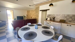 Une cuisine moderne avec un carrelage à motifs géométriques, une table à manger agrémentée de centres de table circulaires noirs, des chaises blanches et un mur de pierre en guise de crédence.